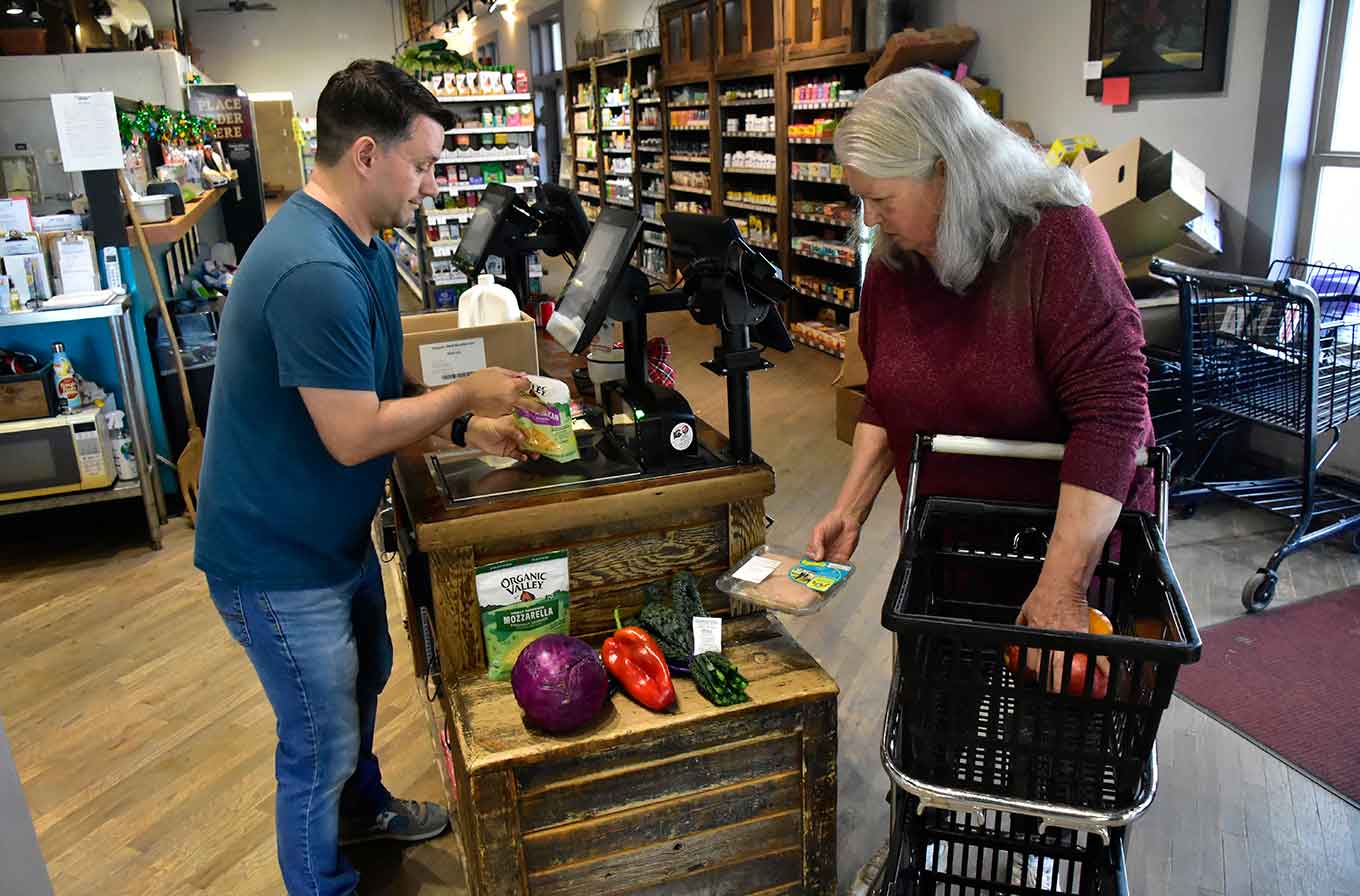 Un cajero escanea productos para una mujer mayor con un carrito de compras en la caja registradora de Simple Foods Market en Del Norte, Colorado.
